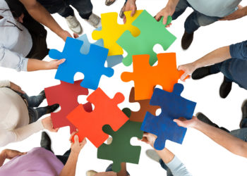 Directly above shot of people holding colorful puzzle pieces in huddle against white background